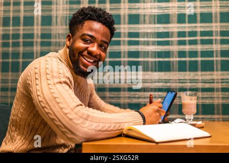 Freelance utilisant smartphone et bloc-notes. Il est assis dans le bar et fait des plans de travail. Banque D'Images