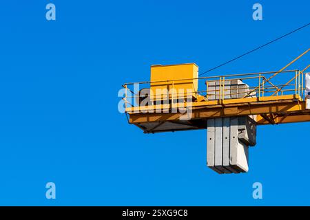 Une grue de construction jaune est vue soulever de grands blocs de béton haut dans les airs, contre un ciel bleu clair et éclatant. L'image capture l'esse Banque D'Images