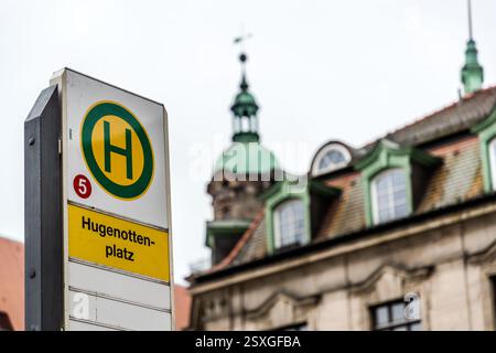 Un panneau d'arrêt de bus marque Hugenottenplatz à Erlangen, en Bavière, Allemagne. La tour à dôme vert de l'Hugenottenkirche (église huguenote) s'élève au-dessus des toits de la vieille ville en arrière-plan. En 1685, le margrave Christian Ernst a permis aux huguenots expulsés de France de s'installer à Erlangen. Environ 1500 d'entre eux sont arrivés dans ce qui n'était alors qu'une petite ville. Banque D'Images