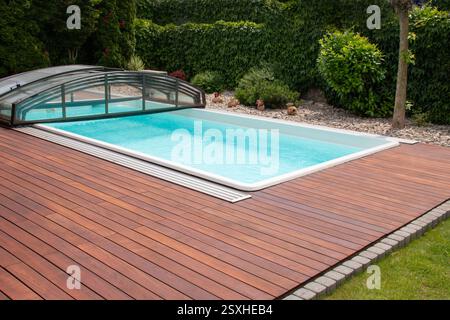 Une belle cour arrière dispose d'une piscine bleue claire avec une couverture en verre rétractable. Terrasse en bois entoure la piscine, avec verdure bien entretenue addin Banque D'Images