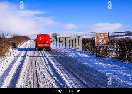 Un facteur optimiste de Royal mail pénètre dans la forêt de Bowland par des routes couvertes de neige fondante par une journée ensoleillée après des chutes de neige fraîches, Lancashire, Royaume-Uni Banque D'Images