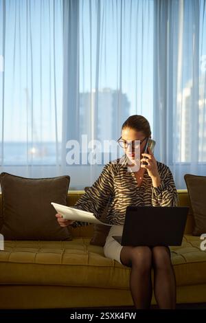 Femme d'affaires travaillant et parlant au téléphone par fenêtre Banque D'Images