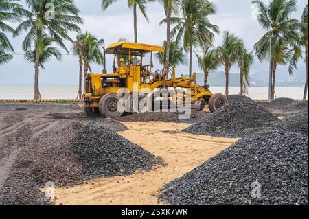 Le bulldozer nivele le gravier sur un chantier de construction sur une plage de sable au bord de la mer et effectue des travaux d'excavation sur la construction en Asie Banque D'Images