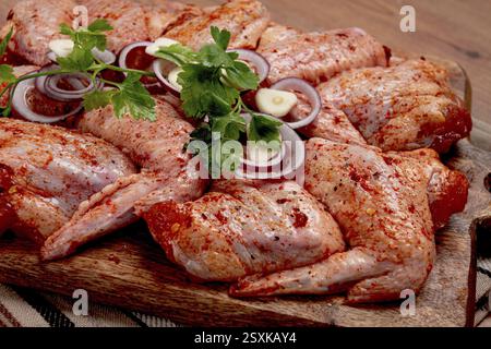 Ailes de poulet, marinées et disposées sur un plateau en bois, prêtes à cuisiner, griller ou cuire, dans une cuisine domestique, il n'y a personne Banque D'Images