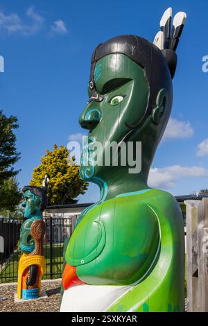 Des sculptures en bois maoris peintes aux couleurs vives d'un homme et d'une femme devant une école à Tauranga, Nouvelle-Zélande Banque D'Images