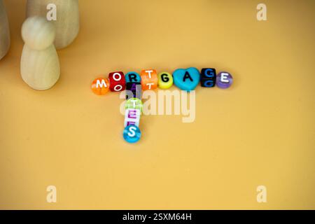 Un arrangement de perles colorées formant le mot hypothèque et les taux accompagnés de figures en bois, symbolisant les concepts financiers, les taux hypothécaires Banque D'Images
