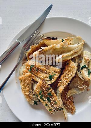 Gratin de fenouil au fromage maison avec parmesan et persil dans une assiette blanche sur fond blanc. Nourriture saine et végétarienne. Directement au-dessus. Banque D'Images