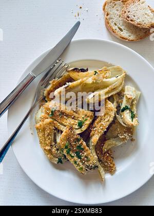 Gratin de fenouil au fromage maison avec parmesan et persil dans une assiette blanche sur fond blanc. Nourriture saine et végétarienne. Directement au-dessus. Banque D'Images