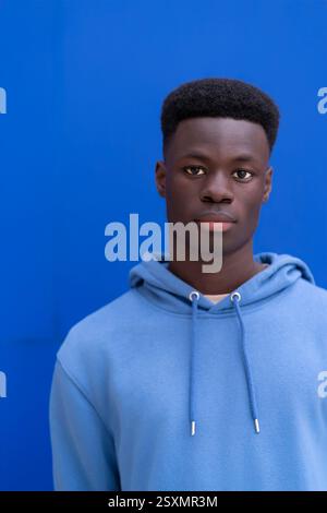 Sérieux jeune homme noir avec sweat-shirt bleu posant devant un fond bleu vif Banque D'Images