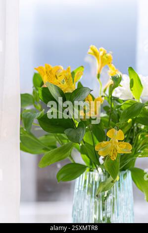 Fleurs d'alstroemeria jaune dans un vase en verre sur le rebord de la fenêtre. Recadrage vertical. Banque D'Images