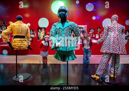 Londres, Royaume-Uni. 25 février 2025. Membres du personnel avec (C)'Blazer with Shorts (tissu vert à fines rayures avec paillettes argentées, porté à l'Alternative Miss World 1986', 1984-5, 'Crash Helmet with paillettes', 1984, et 'Glasses with Eyes', 1984, dans la salle 2 - Club : Would You Let You Yourself In?, lors d'un aperçu de 'Leigh Bowery!', une nouvelle exposition à la Tate Modern dédiée à l'artiste défunt, avec de la fin des années 1980 et 90. L'exposition se déroule du 27 février au 31 août 2025. Credit : Stephen Chung / Alamy Live News Banque D'Images