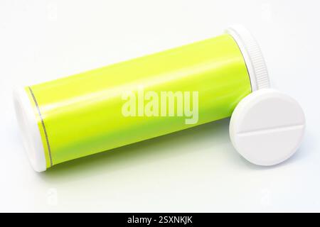 Gros plan d'un comprimé effervescent et de son tube jaune reposant sur un fond blanc, représentant la santé, la médecine et les concepts pharmaceutiques Banque D'Images