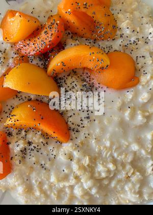 L'image montre un gros plan de flocons d'avoine recouverts de tranches d'abricot fraîches et saupoudrés de graines de pavot. La farine d'avoine a une texture crémeuse, et l'apric Banque D'Images