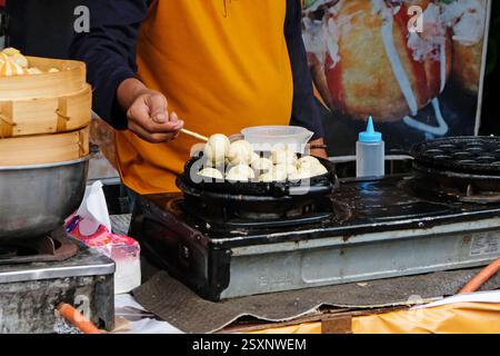 Un homme prépare un Takoyaki sur une poêle chaude. Procédé pour cuire des boules frites avec du poulpe dans la nourriture de rue locale. Banque D'Images