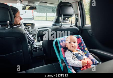 Portrait de bébé riant dans un siège d'auto tandis que mère conduisant une voiture de tourisme. Scène capture le moment de soin et de responsabilité, soulignant l'importance Banque D'Images