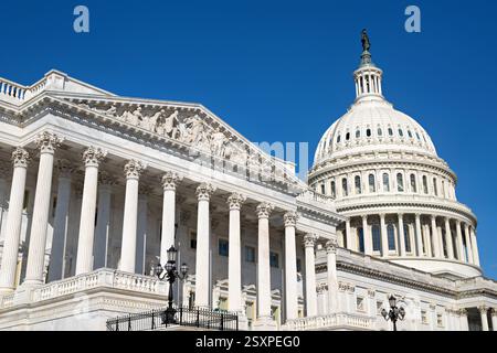 Capitol des États-Unis à Washington DC | WASHINGTON D.C., États-Unis — Une vue en contre-plongée encadre le dôme du Capitole des États-Unis face au fronton de l’aile de la Chambre, dont la sculpture en relief et les colonnes corinthiennes illustrent le design néoclassique du bâtiment. L’extérieur en fonte nervurée du dôme dissimule une coque intérieure et extérieure, une technique d’ingénierie empruntée aux structures à dômes européennes de l’époque. Banque D'Images