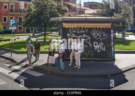 Catane, Italie - 25 février 2025 : touristes et habitants se rassemblent à un arrêt de bus couvert de graffitis à Catane, en Sicile, sous un ciel ensoleillé, près d'un parc. Conc Banque D'Images