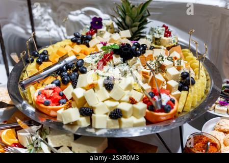 Un plateau de fromages exquis offre une gamme vibrante de fromages, de fruits juteux et d'éléments décoratifs lors d'une réunion festive. Banque D'Images