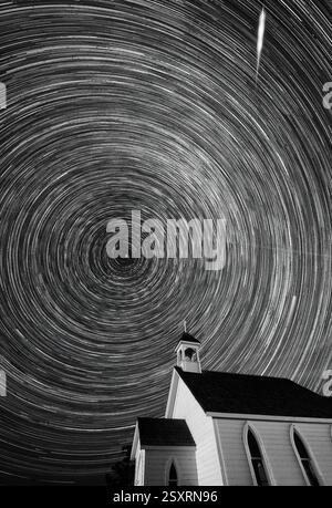 Longue exposition de traînées d'étoiles tournant au-dessus d'une église de campagne la nuit Banque D'Images