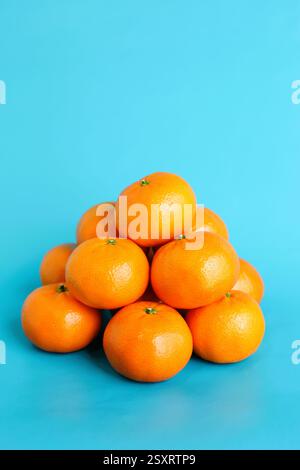 Un tas de mandarines orange empilées sur un fond bleu. Banque D'Images