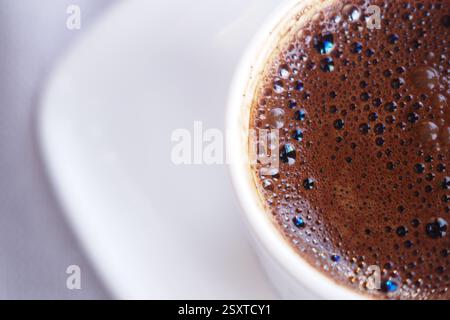 Tasse de café à vapeur sombre placée sur une soucoupe blanche dans un café Banque D'Images