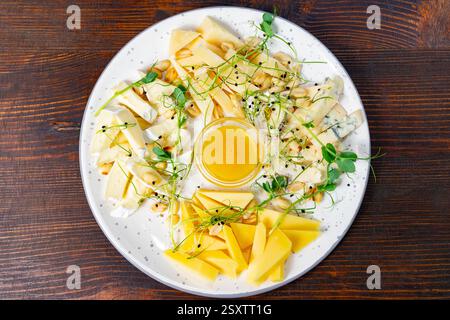 Les variétés de fromage assorties sont habilement disposées sur une assiette ronde. Des herbes fraîches, des pignons de pin et un petit bol de miel ajoutent de la saveur, ce qui fait un délicieux tr Banque D'Images
