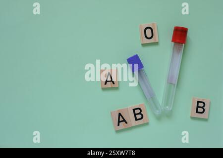 Tubes à essai avec bouchons rouges et violets. Les cubes en bois avec des lettres représentent différents types de sang fond de couleur aigue-marine moyen. Copier l'espace. Banque D'Images