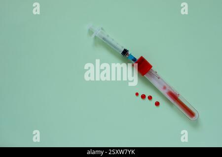 Seringue et tube à essai avec bouchon rouge et sang rouge. Gouttes de sang sur le fond de couleur aigue-marine moyen. Imitant le sang. Banque D'Images