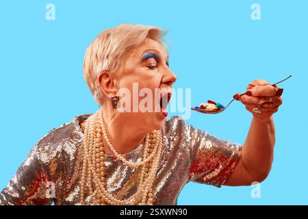 Femme âgée avec fard à paupières bleu vif mangeant cuillère de pilules sur fond bleu vif. Tendances de la santé. Photographie pop art. Banque D'Images
