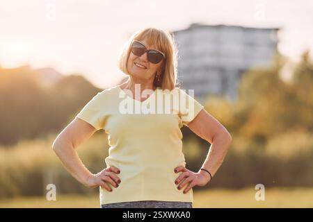 Debout et souriant. Femme senior ayant un bon week-end à l'extérieur sur le terrain à la journée ensoleillée. Banque D'Images