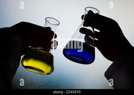 Mains tenant des solutions chimiques colorées dans des béchers de laboratoire Banque D'Images