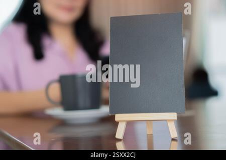 Menu cadre en bois debout sur la table en bois dans le café du restaurant Bar avec la femme floue derrière. Espace pour la promotion marketing textuelle Banque D'Images