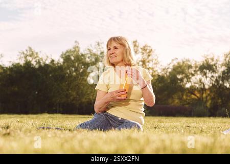 Bouteille orange dans les mains. Femme senior ayant un bon week-end à l'extérieur sur le terrain à la journée ensoleillée. Banque D'Images