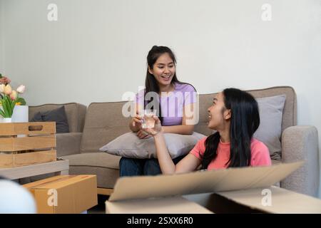 Amis joyeux profitant d'un moment intérieur confortable, partageant des boissons tout en étant assis sur un canapé Banque D'Images