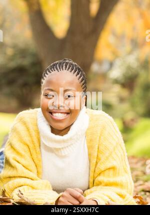 Femme afro-américaine souriante en pull jaune profitant de l'automne à l'extérieur Banque D'Images