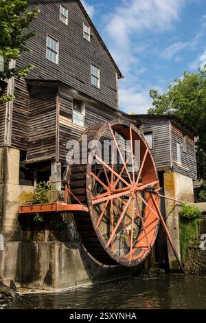 Grande roue en bois est dans l'eau à côté d'un bâtiment. La roue est rouge et a un cadre en bois Banque D'Images