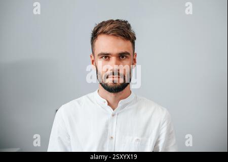 Portrait d'un jeune homme élégant qui se tient à l'intérieur contre le mur. Banque D'Images
