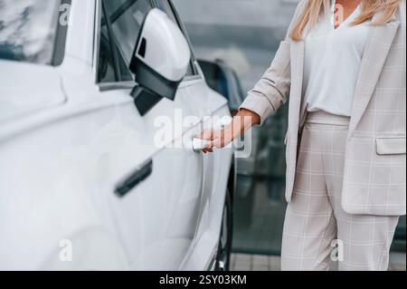 Vue rapprochée de la main ouvrant la porte. Femme en vêtements formels blancs est dans le concessionnaire automobile. Banque D'Images