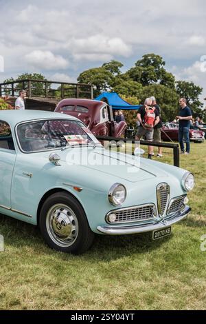 Tarporley, Cheshire, Angleterre, 28 juillet 2024. Une Alfa Romeo Giulia est exposée lors d'une rencontre de voitures anciennes, avec des gens qui socialisent en arrière-plan. Banque D'Images