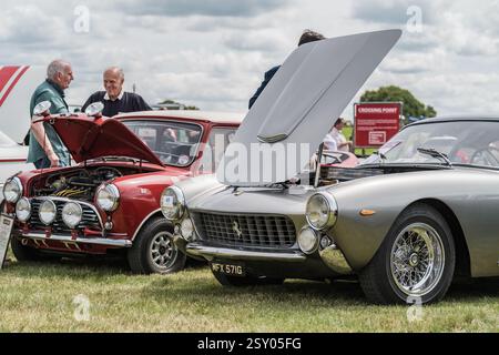 Tarporley, Cheshire, Angleterre, 28 juillet 2024. Les gens regardent une Ferrari 250 GT SWB et une Austin Mini Cooper lors d'une rencontre de voitures anciennes. Banque D'Images