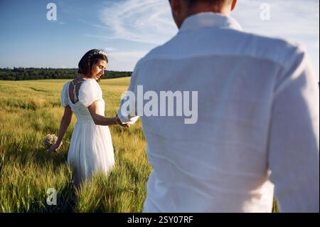 Se tenir par les mains. Couple vient de se marier. Ensemble sur le majestueux champ agricole à la journée ensoleillée. Banque D'Images