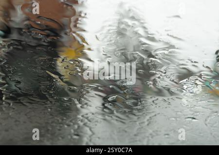 Vue rapprochée floue de la pluie sur le pare-brise d'une voiture, avec la circulation urbaine en arrière-plan, Royaume-Uni. Banque D'Images