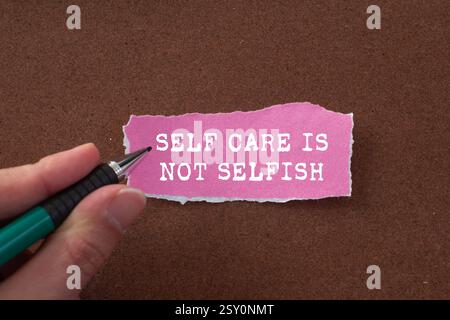 Self Care n'est pas un message égoïste écrit sur papier rose déchiré déchiré sur fond brun. L'autosoin conceptuel n'est pas un symbole égoïste. Copier l'espace. Banque D'Images