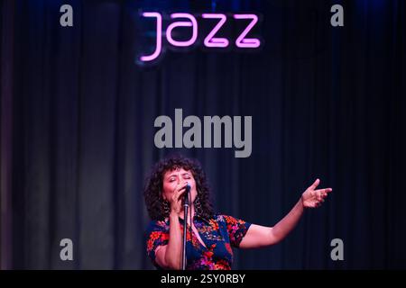 Un chanteur de jazz se produit avec passion sur scène dans une atmosphère vibrante et éclairée par des néons. Banque D'Images