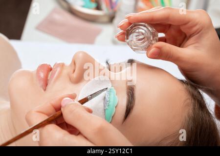 Maquilleur fait la procédure de laminage et de teinture des cils à une belle femme dans un salon de beauté. Extensions de cils. Lifting des cils Banque D'Images