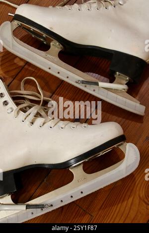 une paire de patins à glace en cuir blanc couché sur le plancher en bois à l'intérieur, se préparant aux sports d'hiver, chaussures de sport pour femmes, style de vie actif et équipement. Banque D'Images