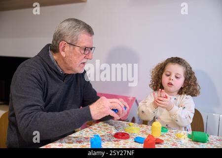 Grand-père et petite-fille jouant avec de l'argile à modeler à la maison Banque D'Images