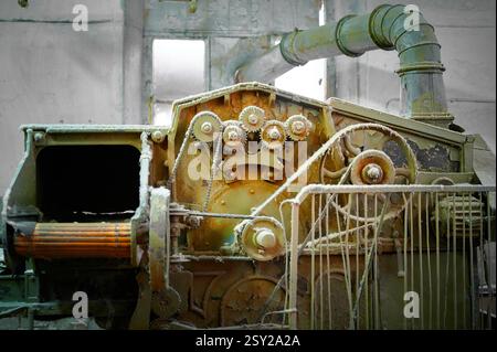 Détails complexes de machines textiles anciennes avec engrenages, courroies et tuyaux dans un environnement d'atelier abandonné Banque D'Images