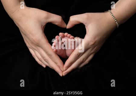 Les mains des parents dans une forme de coeur entourant une paire de petits pieds de bébé, représentant l'amour que les parents ont pour leur nouveau-né. Banque D'Images