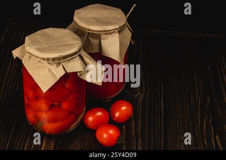 Deux pots remplis de tomates marinées et de concombres sont assis sur une table en bois sombre, mettant en valeur les couleurs vibrantes des légumes conservés, prêts pour e. Banque D'Images